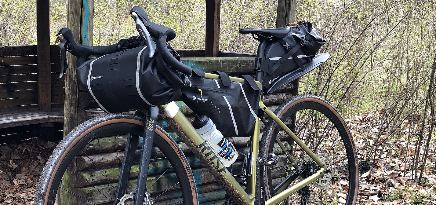 Bikepacking Ein Gravelbike mit Packtaschen lehnt an einer Schutzhütte im Wald.