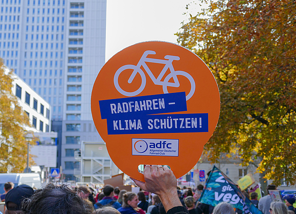 ADFC-Schild mit der Aufschrift "Radfahren - Klima schützen" wird bei einem Klimastreik in die Höhe gehalten.