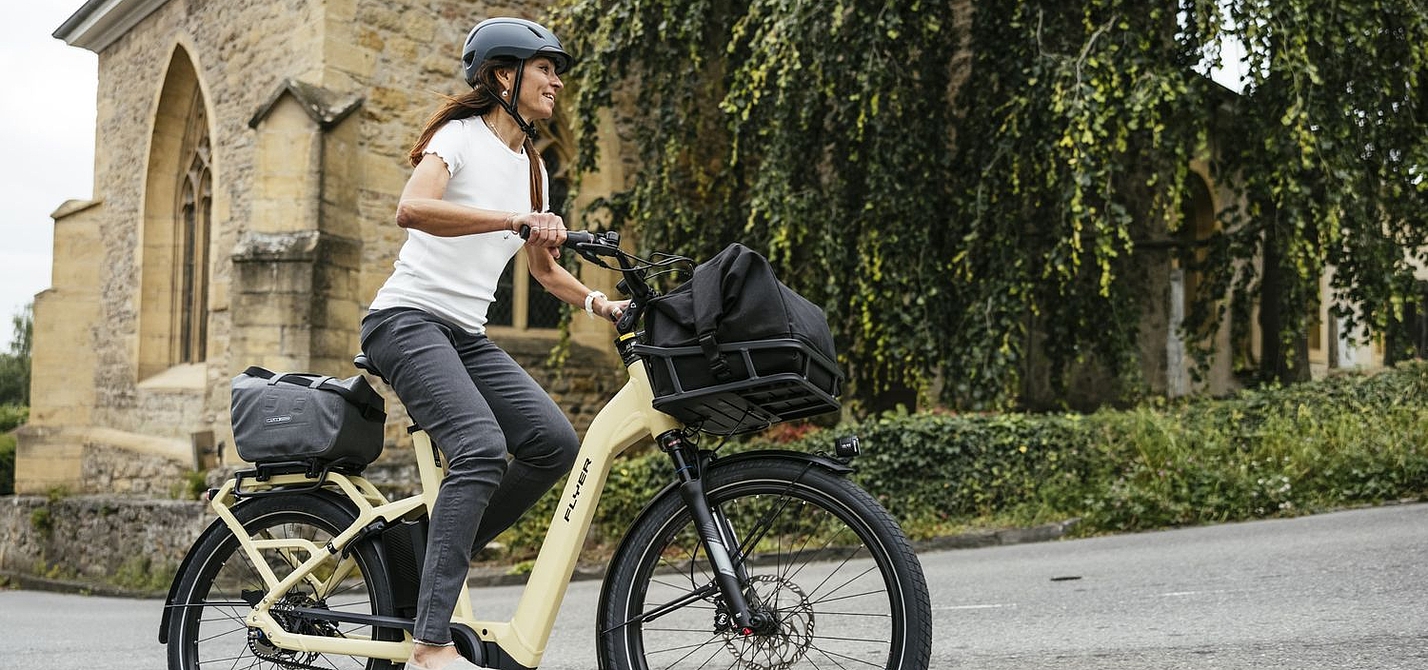 Trekking-Pedelec Fröhliche Frau fährt auf Elektrofahrrad, im Hintergrund eine Kirche.
