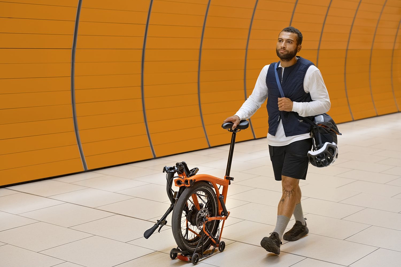 Schieben Ein Mann schiebt ein teilweise gefaltetes Brompton am Sattel durch eine U-Bahn-Station.