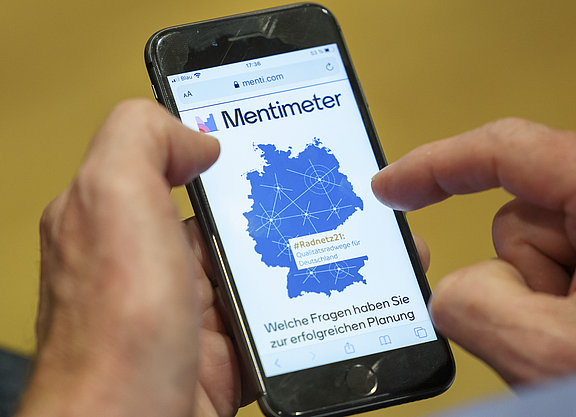 Mann hält ein Handy. Auf dem Handy ist die App Mentimeter zu sehen.