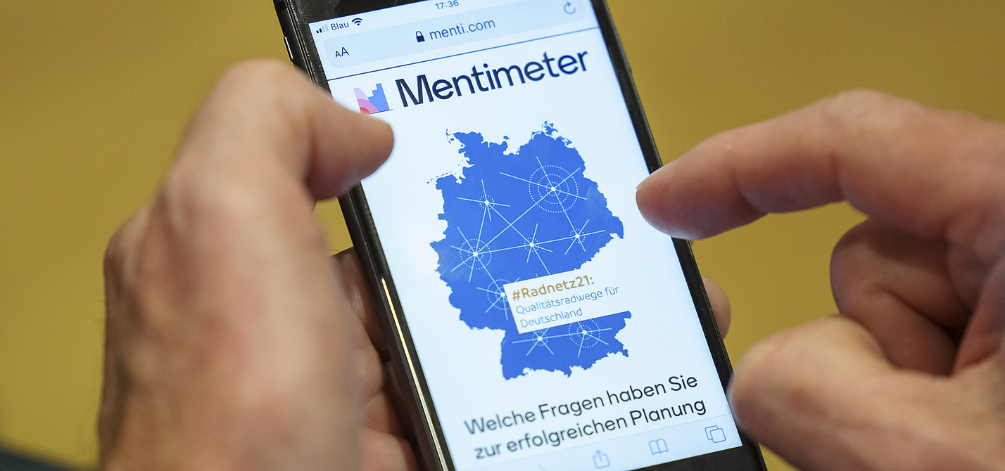 ADFC | Parlamentarischer Abend des ADFC Bundesverband | #Radnetz21: Mann hält ein Handy. Auf dem Handy ist die App Mentimeter zu sehen.