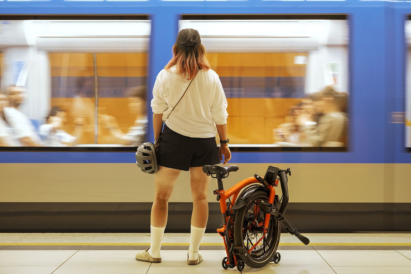 Am Bahnsteig Eine Frau steht am Bahnsteig mit einem gefalteten Brompton G-Line neben sich.