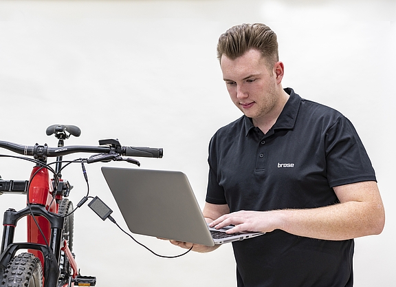 Mann mit Laptop steht neben einem Fahrrad. Das Laptop ist an das Fahrrad angeschlossen. Der Mann liest die elektronisch verfügbaren Daten mit seinem Laptop vom Fahrradmotor aus.